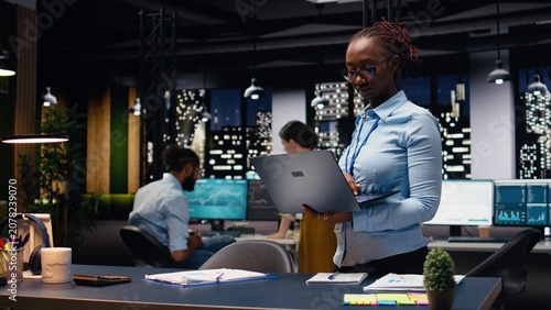 Fotografie Portrait of african american woman in office managing schedules on laptop, organizing calendar appointments and meetings, Jolly young adult compiling company information records and data