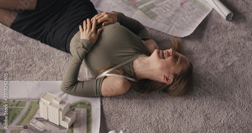 Woman lays on floor with a model and architectural plans, showing her excitement and focus on the project at hand