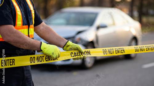 Police officer cordoning off a traffic accident scene with caution tape, restricting public access to a damaged vehicle after a traffic accident, close up of hands