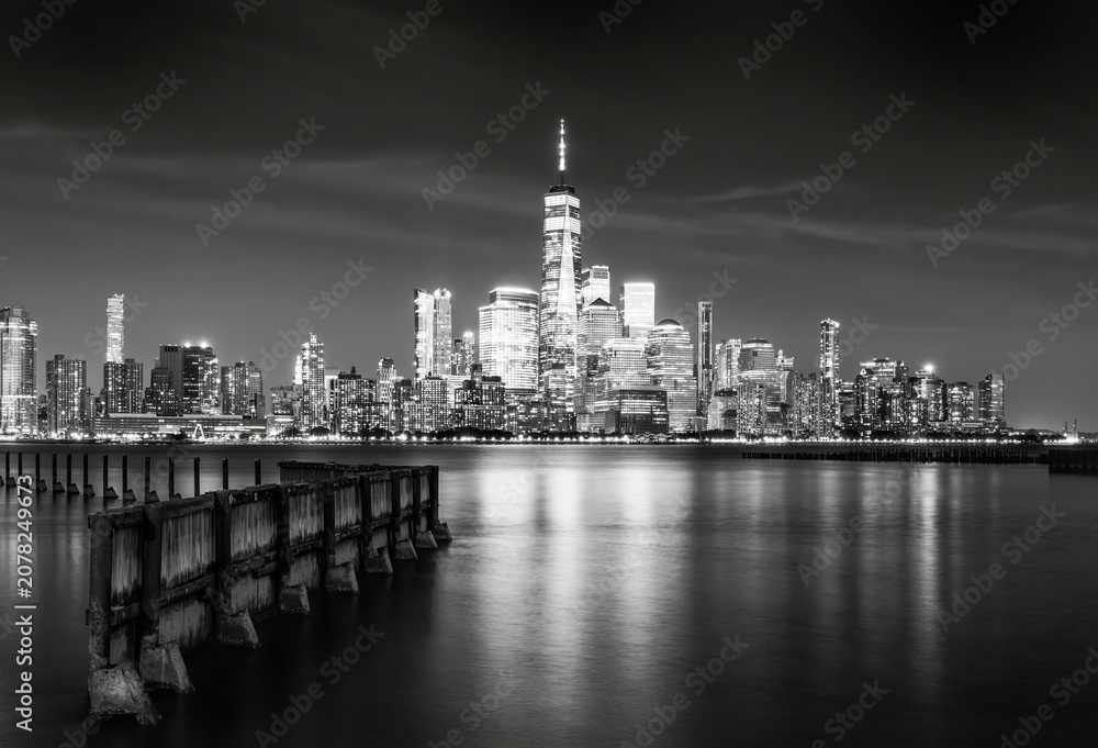 Fototapeta premium Black and white long exposure of the Lower Manhattan skyline and World Trade Center skyscrapers reflected in the Hudson River at night, New York City, USA