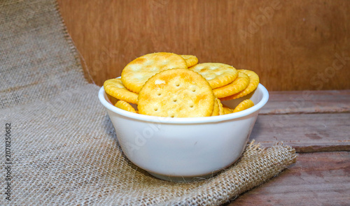 Fotografie Round salty crackers served on a plate in a white bowl on a wooden table with jute sack