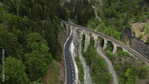 View of the historic stone railway viaduct crossing a dramatic alpine gorge with mountain road and snow-covered peaks near Chamonix in the French Alps