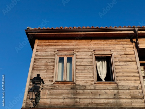 Old Wooden House with Window Frames and Curtains Under a Clear Blue Sky.