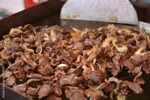 Brazilian sun dried beef cooking with onions on a hot griddle close up