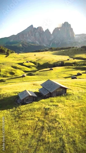 Aerial view of camping tents in golden meadow with dramatic mountain backdrop at sunrise