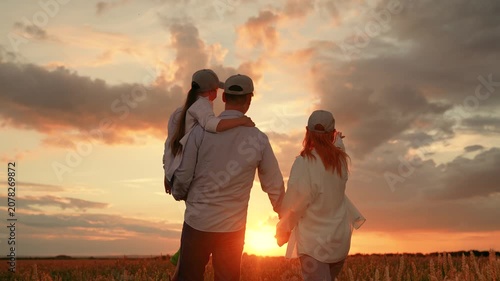 Kid daughter sits in father arms walk hand in hand with mother wheat field sunset. Happy farming family with child strolls wheat field. Farmers, dad mom child girl outdoors together, enjoying, sun sky