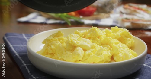 Close up of chef transferring fluffy homemade scrambled eggs from a frying pan onto a white serving plate. Fresh creamy eggs are carefully plated for a delicious homemade breakfast in a cozy kitchen.