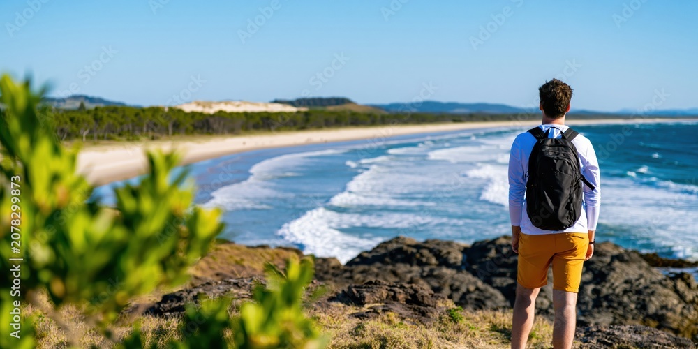 Naklejka premium Man hiker with backpack standing on a rocky cliff overlooking the ocean beach view