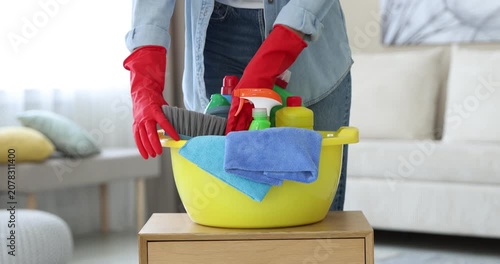 Woman putting plastic basin with cleaning products and supplies on wooden table in room, closeup