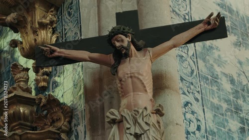 Carved crucifix of Jesus Christ on a black cross beside blue azulejo tiles inside a church