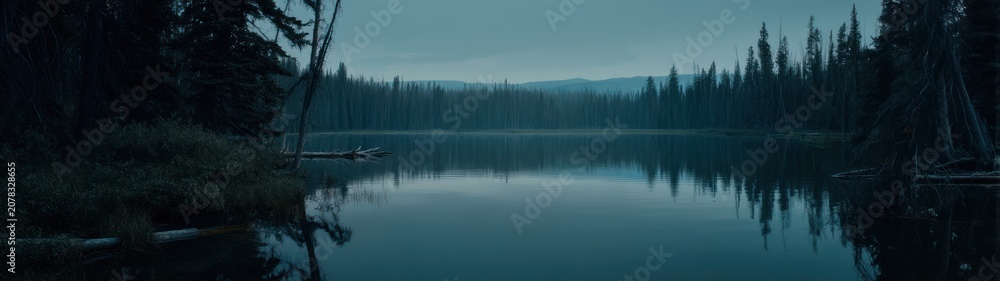 Fototapeta premium Tranquil lake scene with reflections of forest and overcast sky at dusk