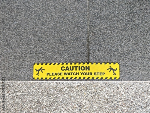 Fotografie Yellow caution sign warning people to watch their step on a textured floor