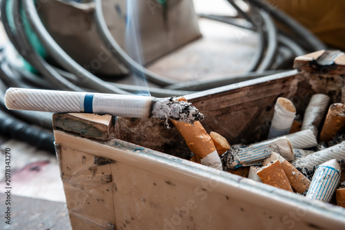Konstfotografi Burning cigarette with smoke in dirty ashtray full of butts