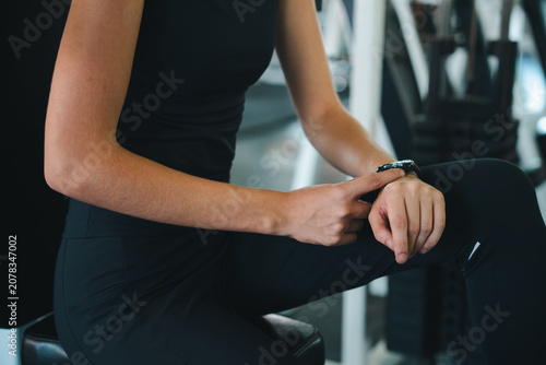 Woman fitness gym smartwatch wrist exercise workout sportswear health technology, woman checking smartwatch wrist during gym workout, wearing black sportswear fitness center with exercise
