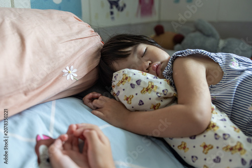Obraz na plátne Close-up portrait of a sleeping Asian toddler girl resting peacefully in bed with a printed bolster pillow