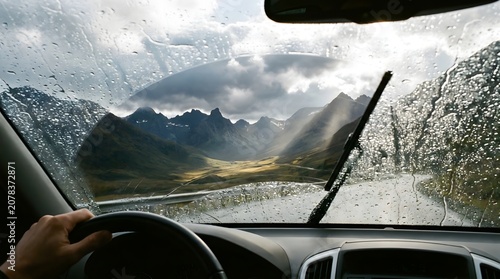 Driving through a scenic mountain landscape during a rainstorm with wipers clearing the windshield.