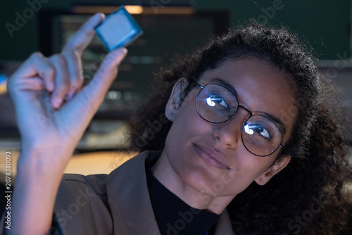 Cuadro en lienzo An engineer holds a tiny silicon microchip between his fingers, inspecting it closely in a blue lit technology lab, during a collaborative evening project session amid the soft hum of a