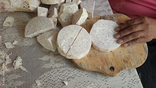 Hands cutting rustic sweet potatoes with dirt into pieces on a wooden table