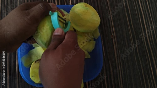 Hands peeling ripe yellow mangoes using a rustic kitchen knife