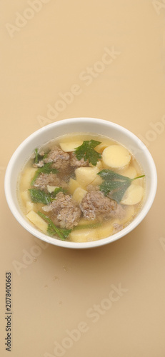 High angle view of clear soup with egg tofu and minced pork in a white bowl.