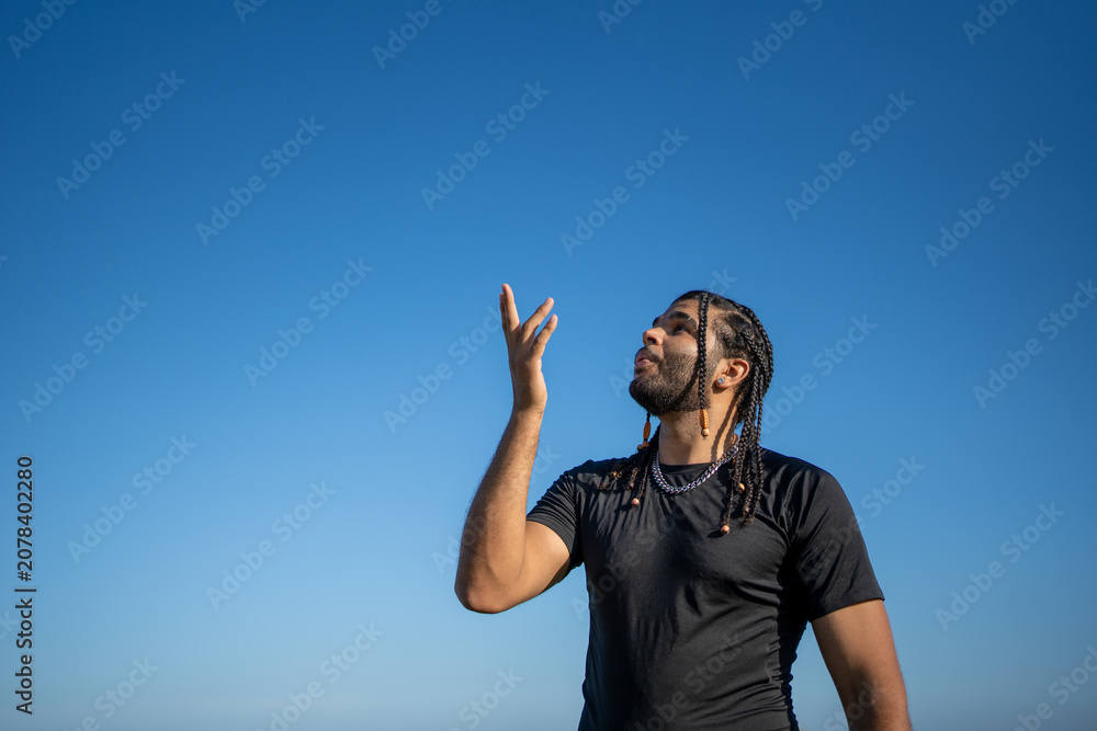 Fototapeta premium Young man looking up with hand raised feeling freedom