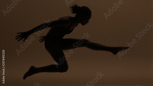 Silhouette of dancer mid-leap against warm, hazy background.