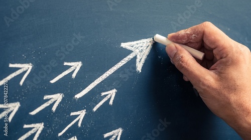 A hand drawing a large upward arrow with chalk on a blackboard, symbolizing progress and leadership.