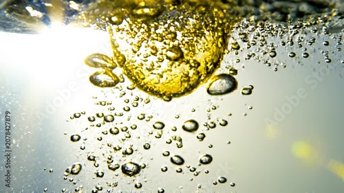 Close-up photography of rising golden air bubbles in liquid creating a bright sparkling underwater effect with light reflections