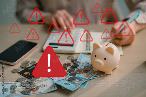 Financial crisis concept with warning triangle sign icons over money and piggy bank on desk