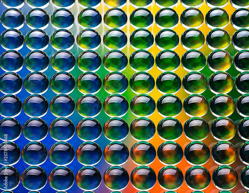 Grid of Transparent Spherical Beads Reflecting Rainbow Gradient from Blue to Red Demonstrating Light Refraction, Color Dispersion, and Artistic Symmetry concept.