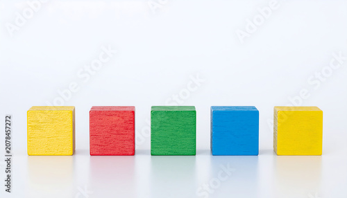 Row of Five Colorful Wooden Cubes in Yellow, Red, Green, Blue, and Yellow on White Surface Representing Symmetry, Variation, and Educational Design with Geometric Shapes.
