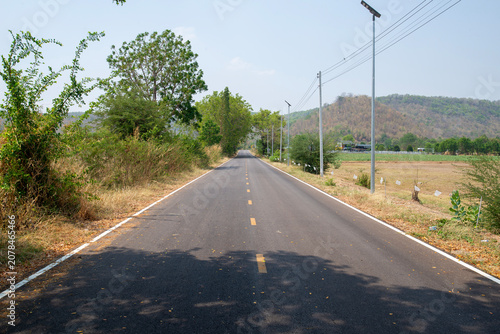 Asphalt rural road leads straight to the mountains ahead.