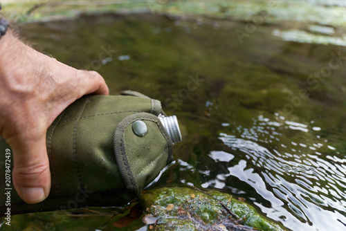 Cuadro en lienzo Hand filling a military style canteen with fresh water from a natural stream, em