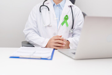 doctor using laptop and report notes on notebook. lime Green Ribbon for concept of May Celiac Awareness month, Lyme disease, September Lymphoma, Mental Health Awareness month and October Liver cancer