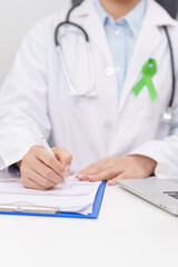 doctor using laptop and report notes on notebook. lime Green Ribbon for concept of May Celiac Awareness month, Lyme disease, September Lymphoma, Mental Health Awareness month and October Liver cancer