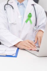 doctor using laptop and report notes on notebook. lime Green Ribbon for concept of May Celiac Awareness month, Lyme disease, September Lymphoma, Mental Health Awareness month and October Liver cancer