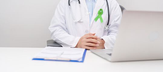 doctor using laptop and report notes on notebook. lime Green Ribbon for concept of May Celiac Awareness month, Lyme disease, September Lymphoma, Mental Health Awareness month and October Liver cancer