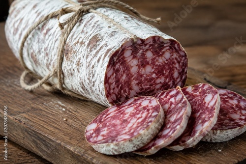 Thick French saucisson on rustic board with white mold, tied with twine, artisanal feel.