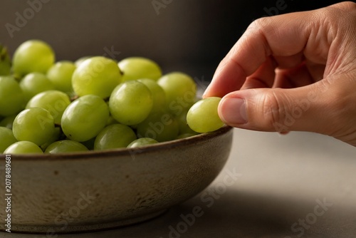 A single green grape being taken from a full fruit bowl, soft light.