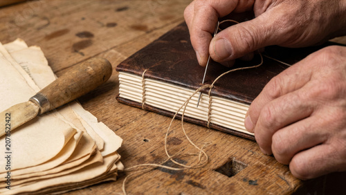 Macro view of English bookbinder hand sewing cotton signature pages into dark leather spine photo