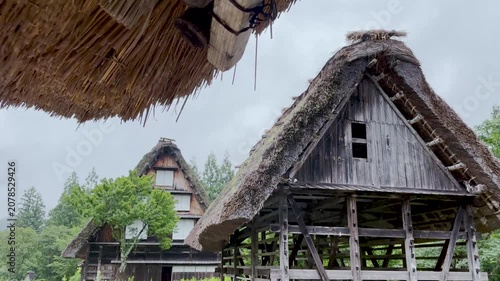 Traditional Gassho-zukuri houses in rainy Shirakawa-go village with misty mountains, slow tilt down shot, Japan