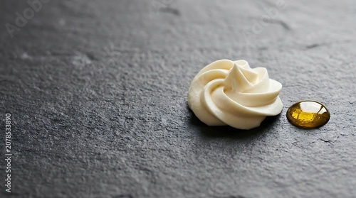 Swirl of white face cream and amber oil drop on dark stone surface