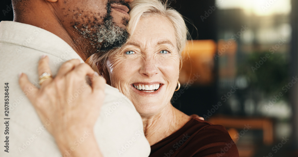 Fototapeta premium Hug, smile and interracial couple in home with trust, connection and relationship wellness. Mature man, woman and embrace with partner for love, security and commitment together with funny portrait