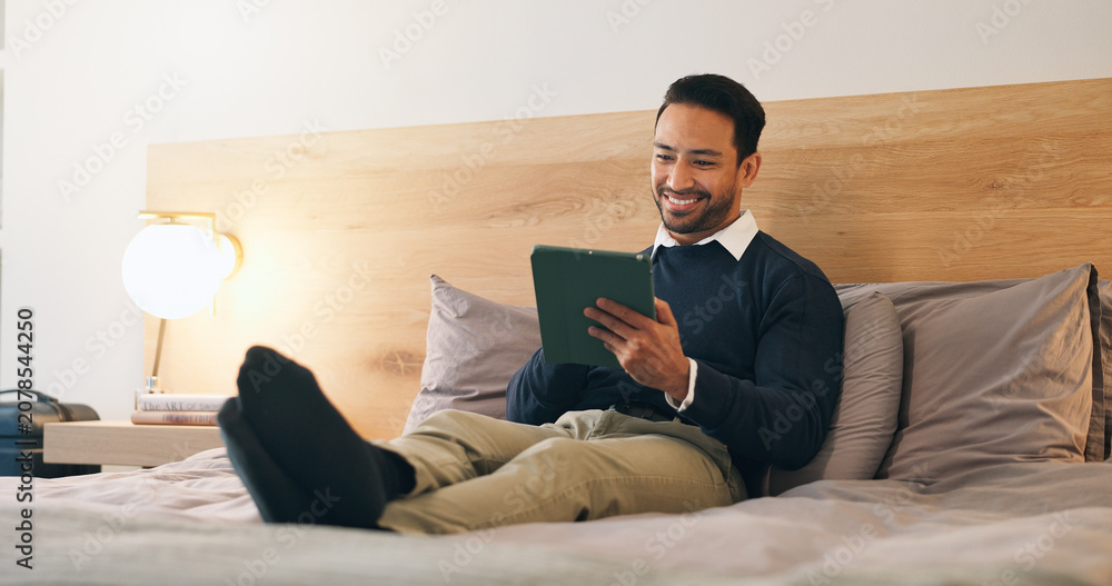 Fototapeta premium Business, man and relax in hotel room with tablet, booking flight and website for work trip. Smile, male person and employee at motel with tech, departure schedule and reservation checkin for travel