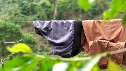 Close-up view of wet laundry hanging with a clothesline against a background of lush green trees.	