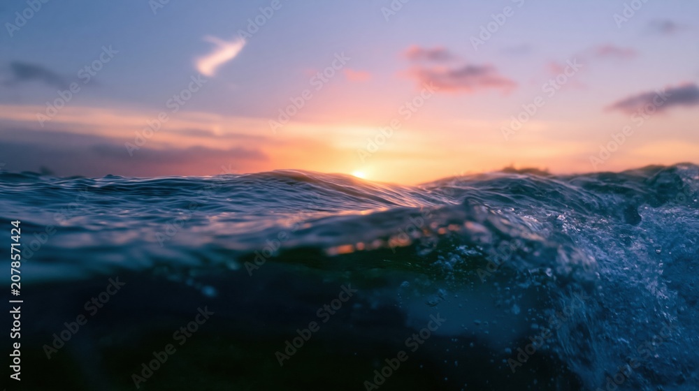 Fototapeta premium Split horizon view of a rippling ocean wave at sunset, featuring a glowing apricot sky and dark subsurface water for travel and nature concepts
