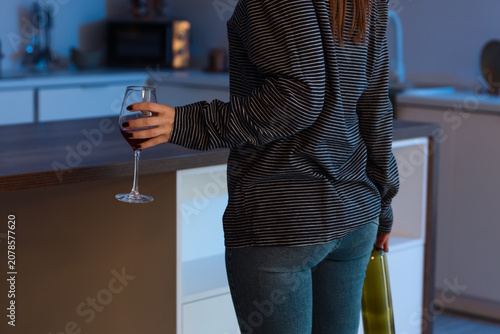 Photos Woman holding wine glass and bottle in kitchen at night