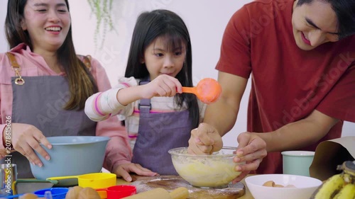 Happy Asian family mixing flour dough together to bake dessert in kitchen
