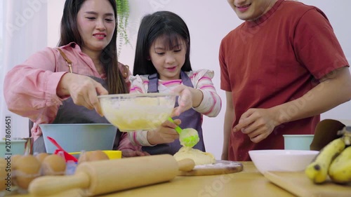 Asian girl kneading dough with flour on wooden board with parents assisting.