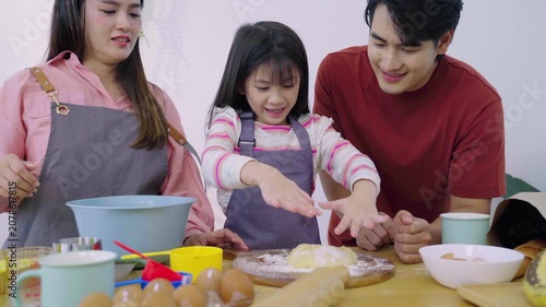 Asian girl kneading dough with flour on wooden board with parents assisting.
